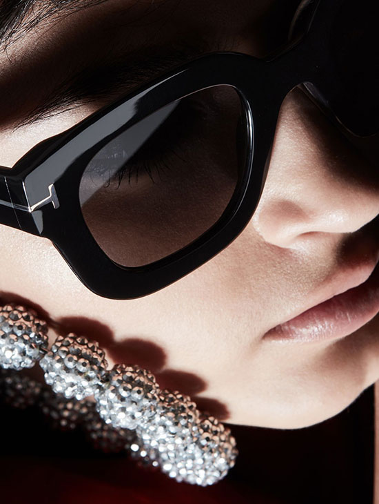 a close up shot of a woman's face who is wearing thick-rimmed tom ford sunglasses and a diamond earring.